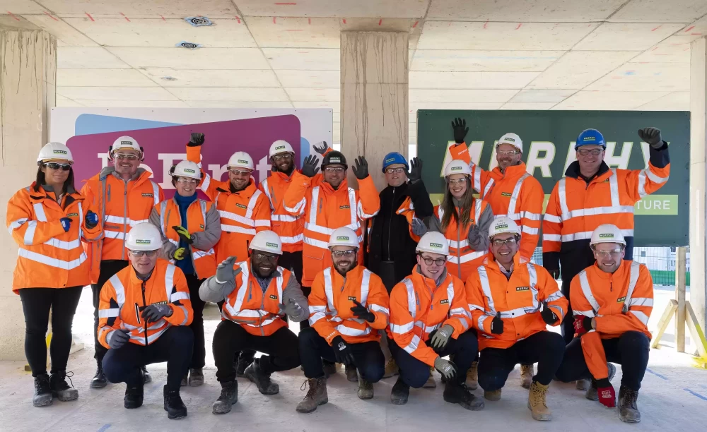 A group of Murphy employees wearing high visibility uniform and helmets smiling with their hands in the air.