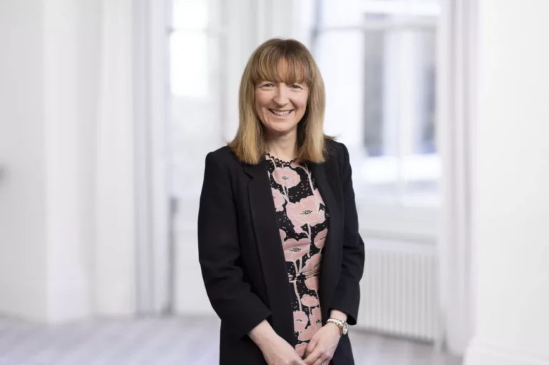 A woman in business dress standing next to a window in a bright room posing for a professional photo.