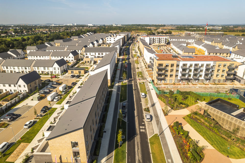 An aerial view of a residential area with houses, fields, roads and cars.