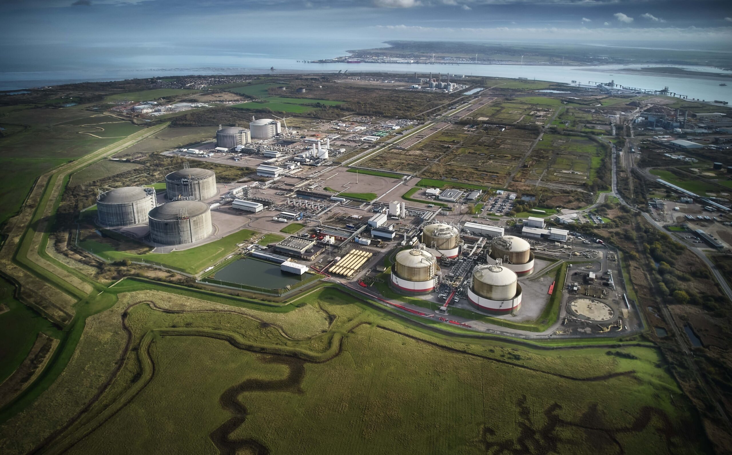 An aerial view of a Liquefied Natural Gas terminal surrounded by fields with a shoreline in the background.