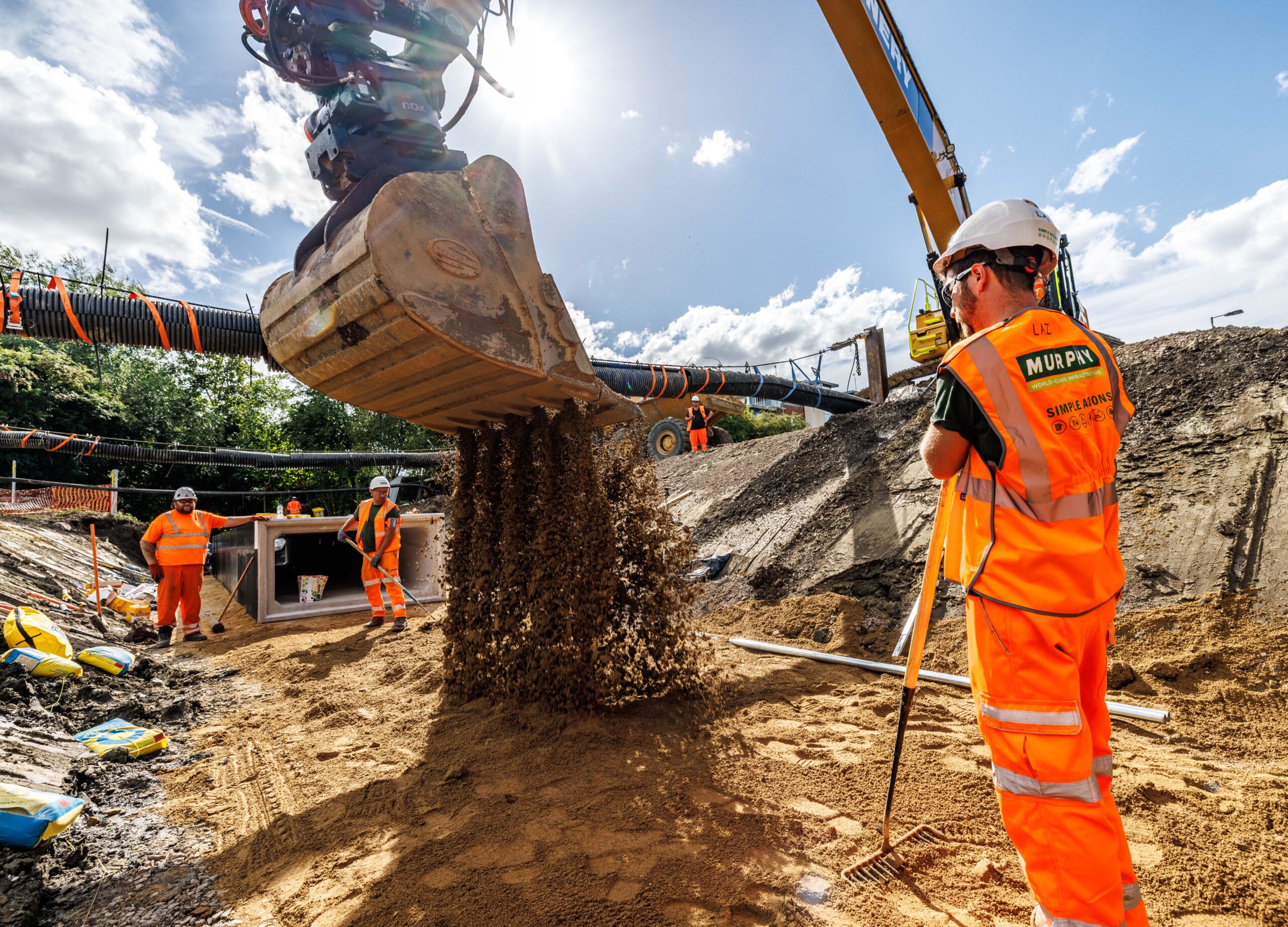 A construction site with a large construction vehicle digging up the ground surrounded by Murphy employees in safety uniform.
