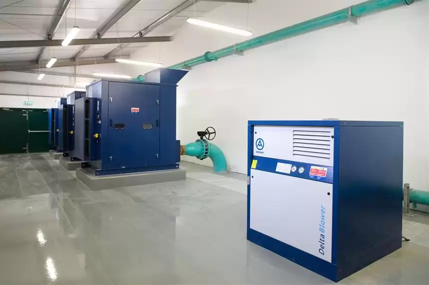 The inside of a wastewater treatment plant with large machines and green pipes lining the walls.