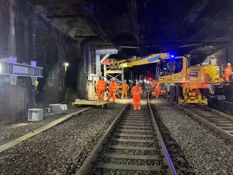 People in safety uniform and Murphy branded construction vehicle working on some train tracks.