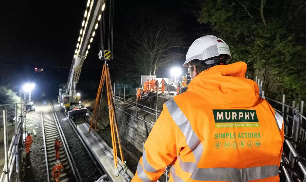 A group of people wearing Murphy safety clothing and a helmet working on a railway track project at night.