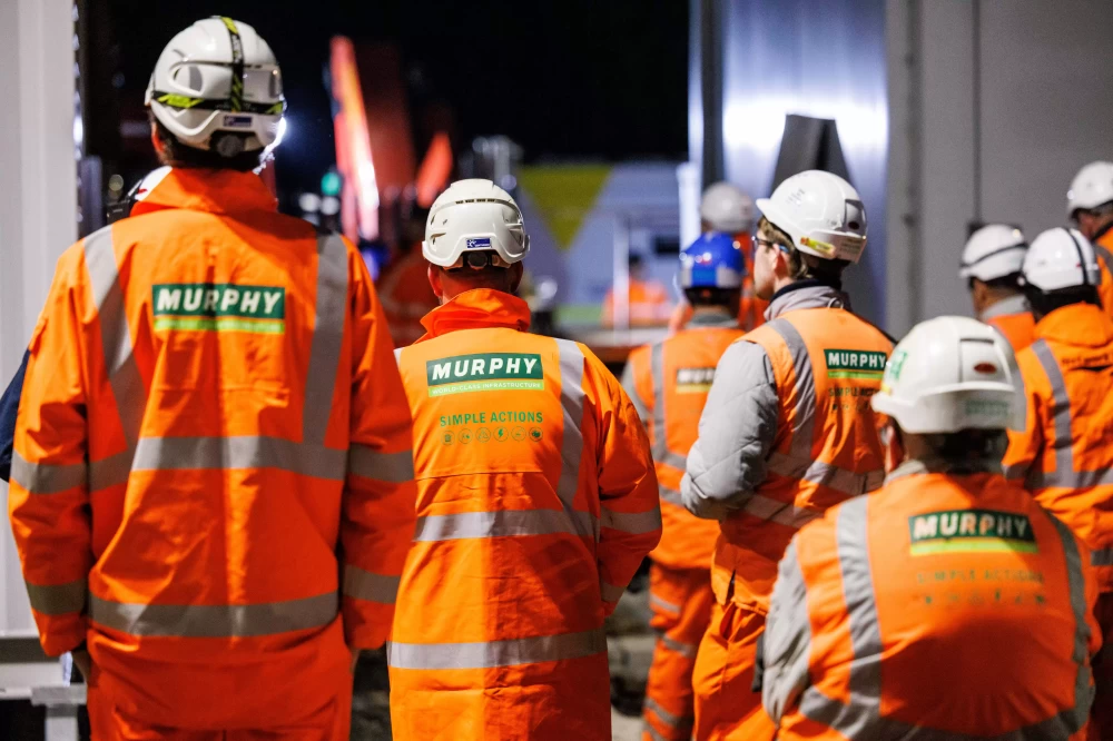 A group of people wearing helmets and Murphy branded high-visibility jackets and trousers facing away from the camera.