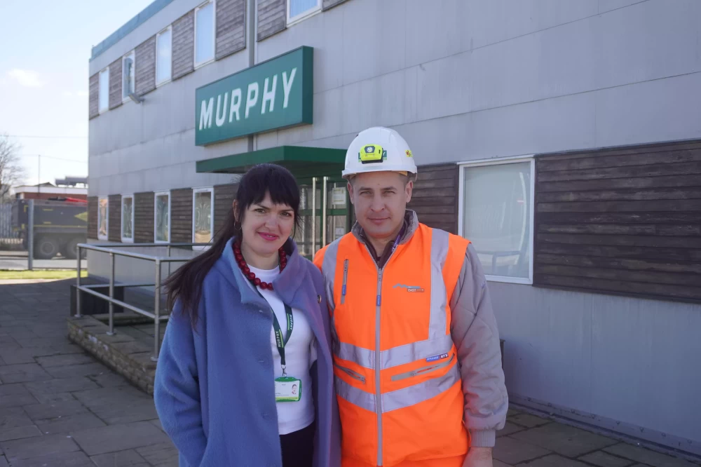 Two people stood outside a building with Murphy sign smiling for a photograph.