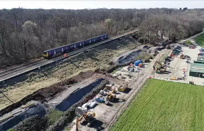 An aerial view of a train on train tracks next to a construction site surrounded by trees.
