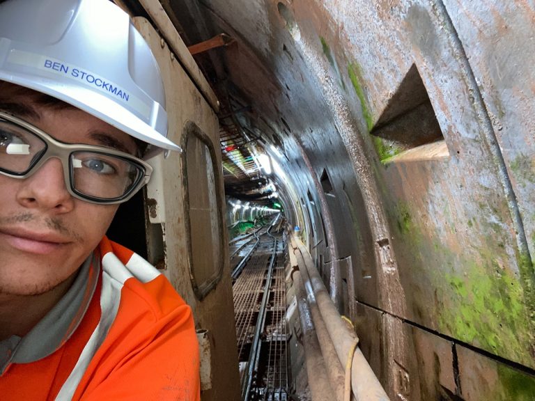 A close up photo of a person in a high-visibility jacket and a helmet in a train tunnel.