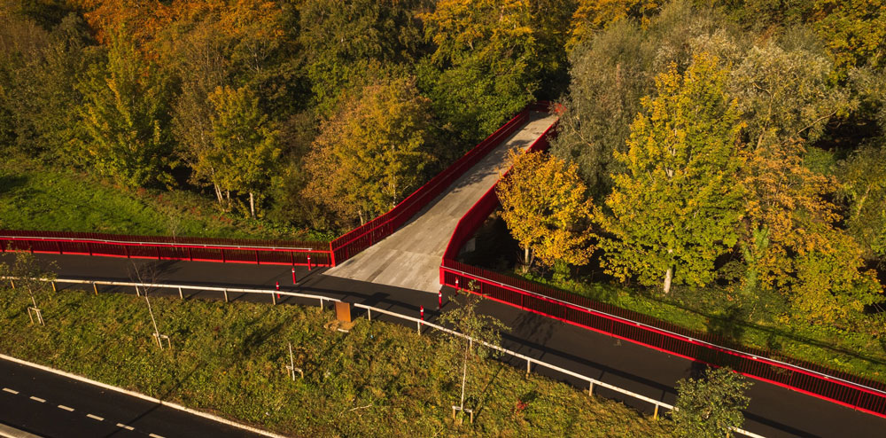 An aerial view of a red bridge surrounded by trees next to a road.