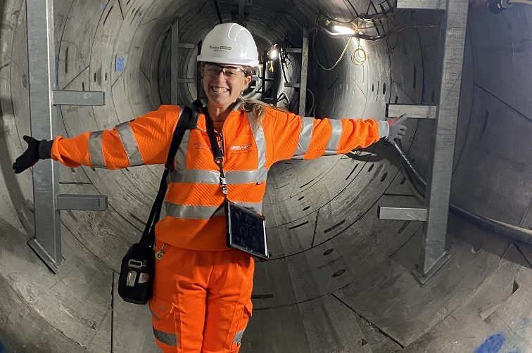 A worker wearing an orange Murphy uniform and a helmet stood smiling in a tunnel with their arms outstretched.
