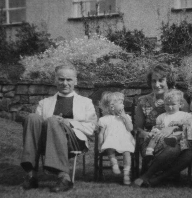 A black and white image of a man, woman, and two children sat on chairs in a garden.