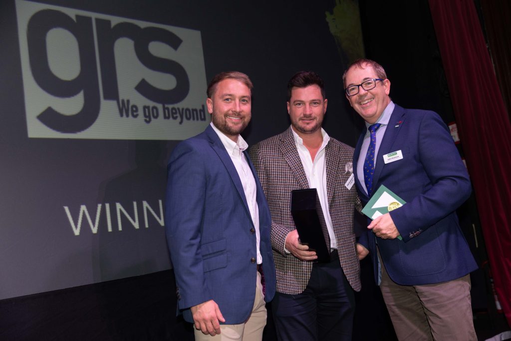 Three people in business dress posing for a photo at an awards ceremony.