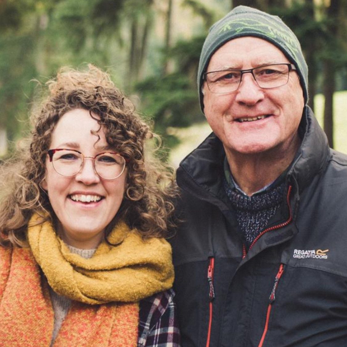 A man and woman outdoors wearing winter clothing with trees in the background.