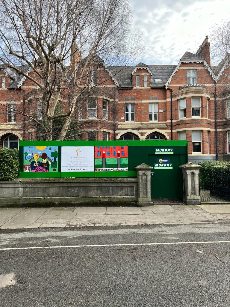 A building undergoing work by Murphy, showing decorative community-made artwork on the panels at the boundary.