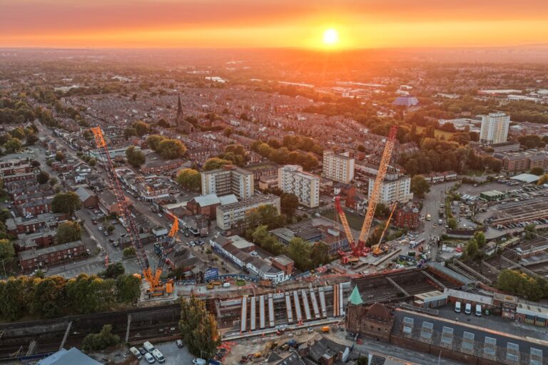 An aerial view of a built up area with train tracks and cranes with the sun setting in the background.