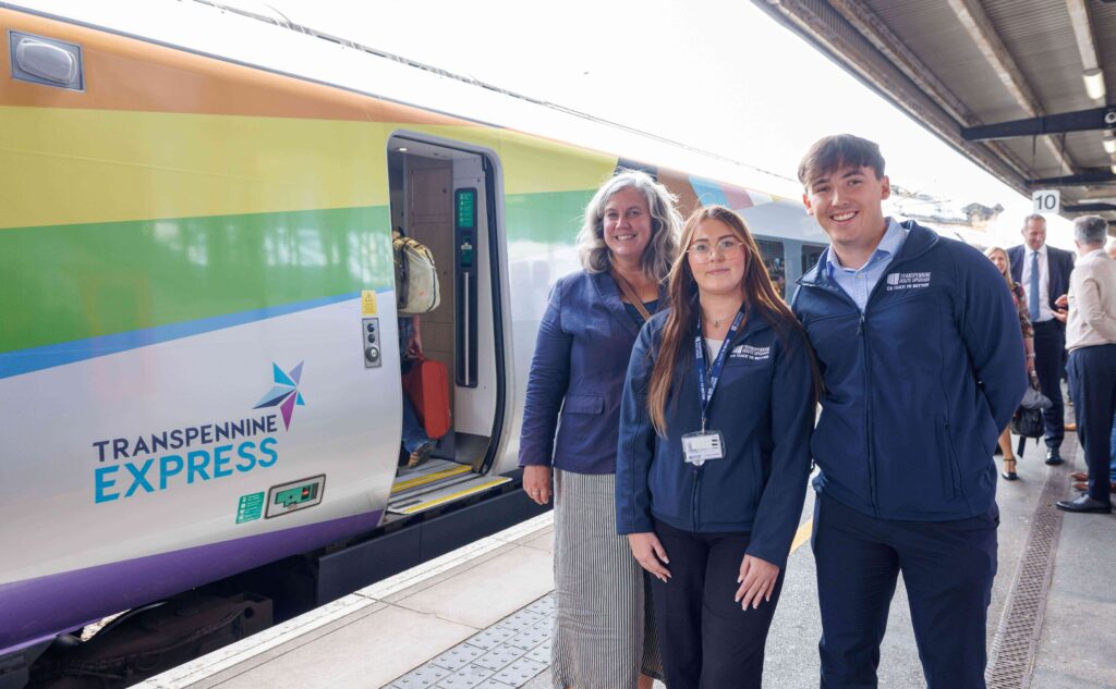 Three people stood smiling next to a train at a station.