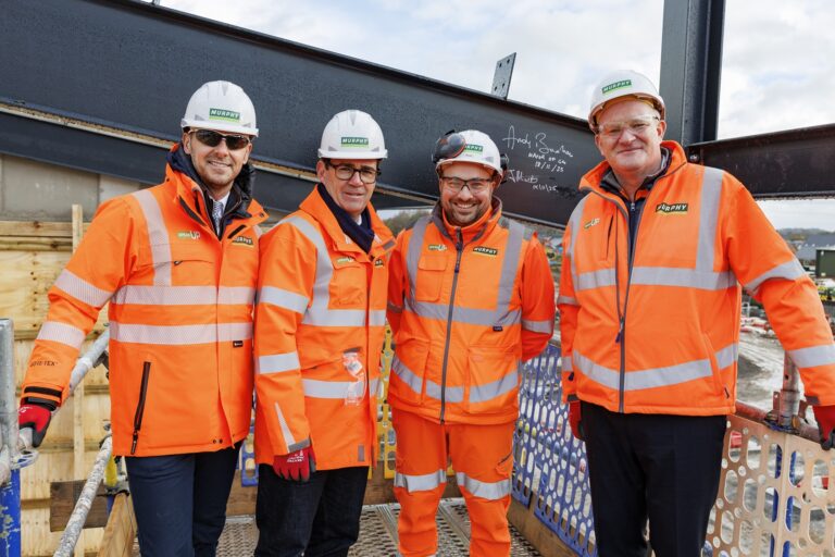 Four Murphy employees dressed in orange high-visibility clothing with safety helmets at a construction site.