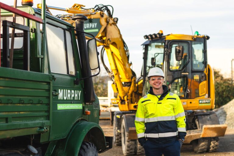 A person wearing safety uniform stood in front of a Murphy branded construction vehicle.