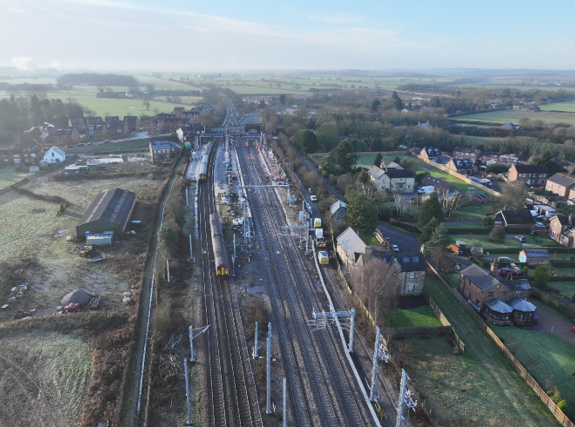 The view of a railway construction site from above surrounded by fields and houses on a bright day.