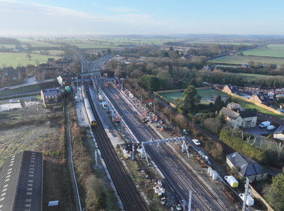 An aerial view of a railway route construction site surrounded by fields and houses.