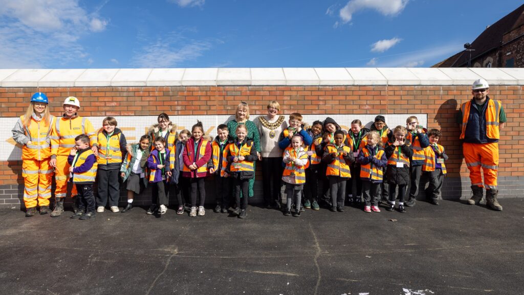 A group of children and adults wearing orange high-visibility uniforms stood against a wall smiling.
