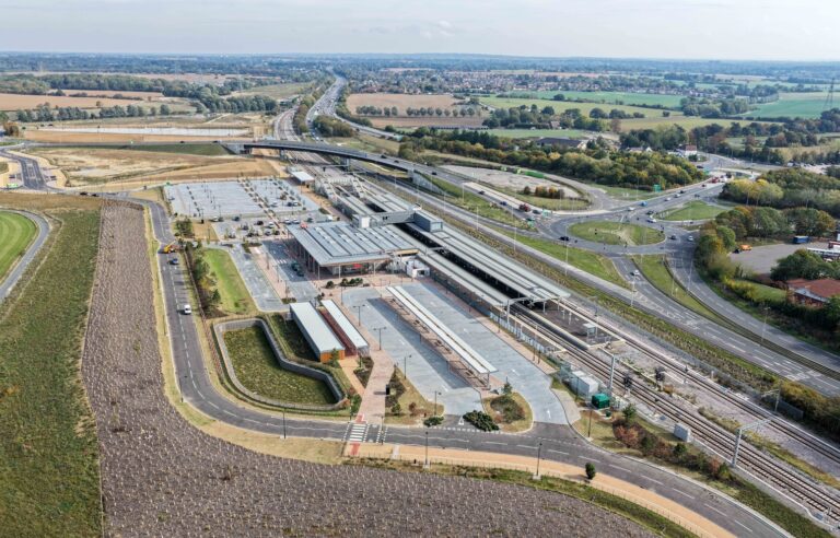 A view of a train station from above in the daytime surrounded by roads and fields.