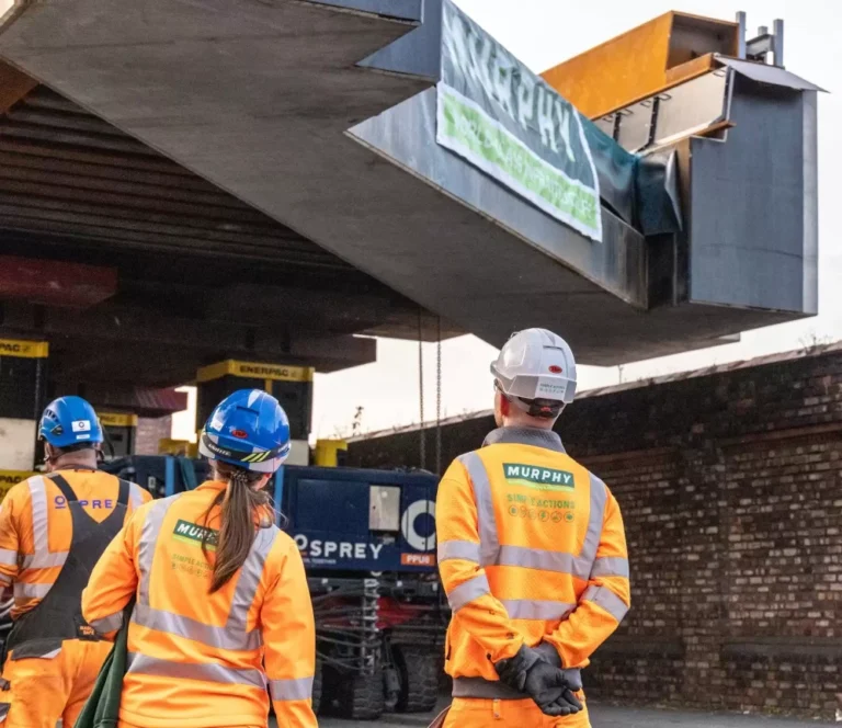 Three people in Murphy uniform looking up at bridge with the Murphy logo on it.