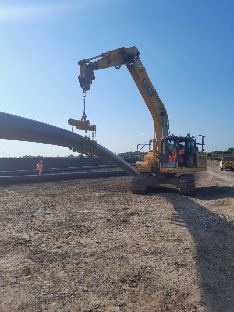 A Murphy construction vehicle lifting a large pipe at a construction site.